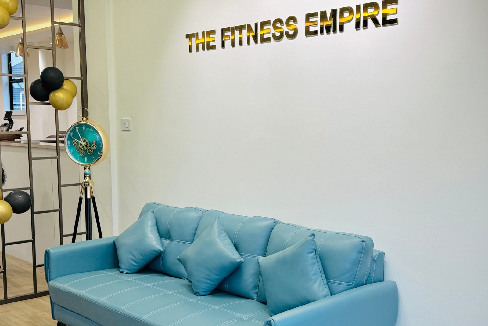 Members lounge — teal sofa under gold THE FITNESS EMPIRE wall